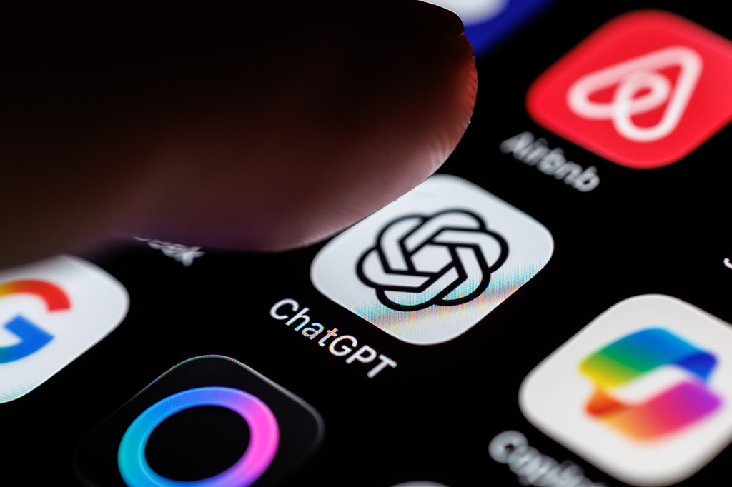 Um dedo pressiona a tela de um smartphone, focando no ícone do aplicativo ChatGPT, que exibe um logo branco e preto com um nó estilizado. Outros ícones de aplicativos como Google e Airbnb estão visíveis ao redor, em um fundo escuro