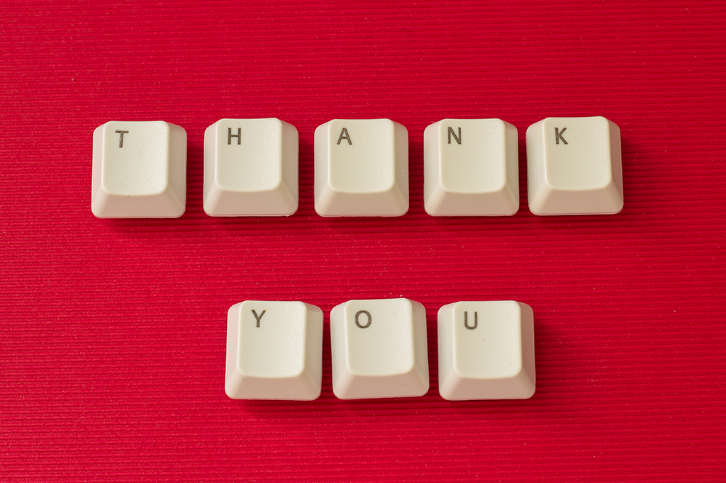 Teclas brancas de teclado formam a frase THANK YOU em duas linhas sobre um fundo vermelho texturizado